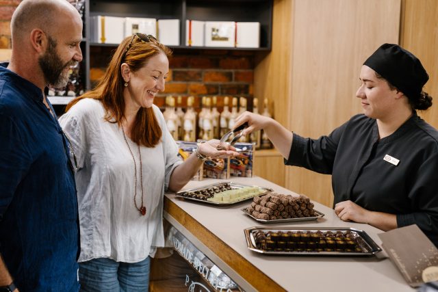 The House of Anvers chocolate factory - a couple having a taste test of assorted chocolates. An employee handing a chocolate to the woman.