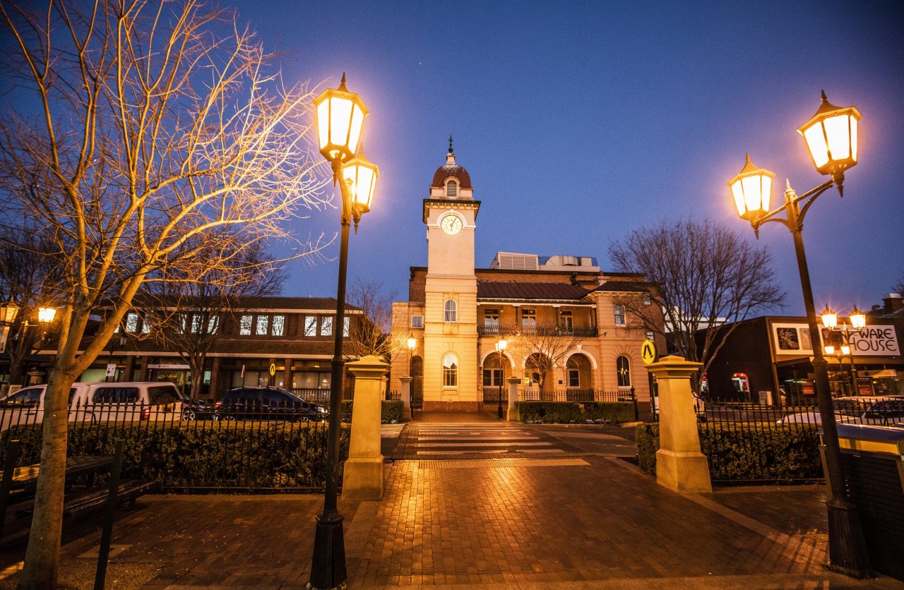 Street view of the Dubbo Clock Tower at night time, with light posts being lit.