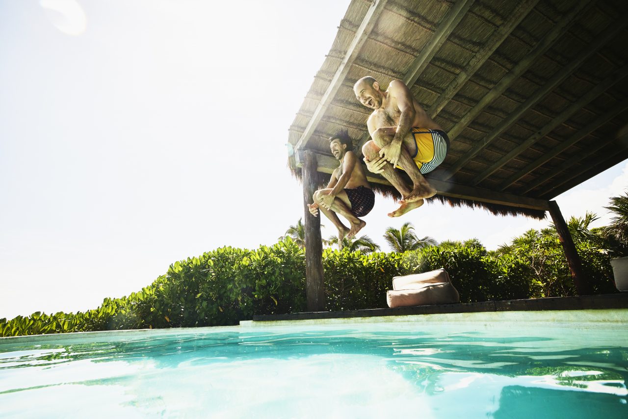 Wide shot of gay couple jumping into pool at luxury tropical villa while on vacation