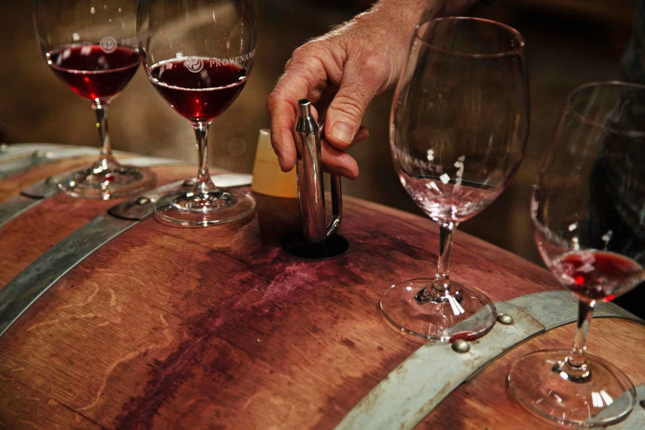 Four wine glasses on top of a wooden barrel with wine