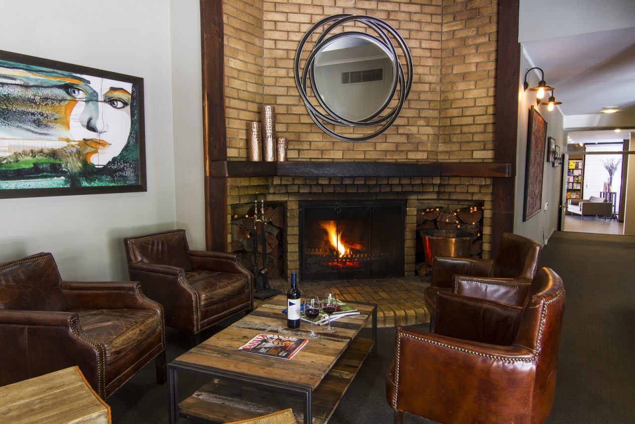 A lounge room in a hotel with lounge chairs, coffee table with wine, and a warm cozy fire in the side of the room.