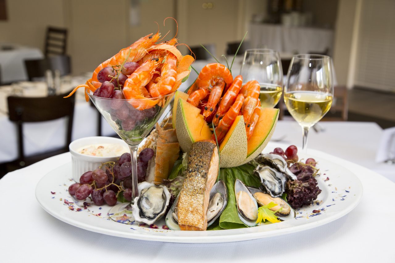 A seafood platter with prawns in cocktail glasses, salmon, oysters, and yummy fruits on a dish.