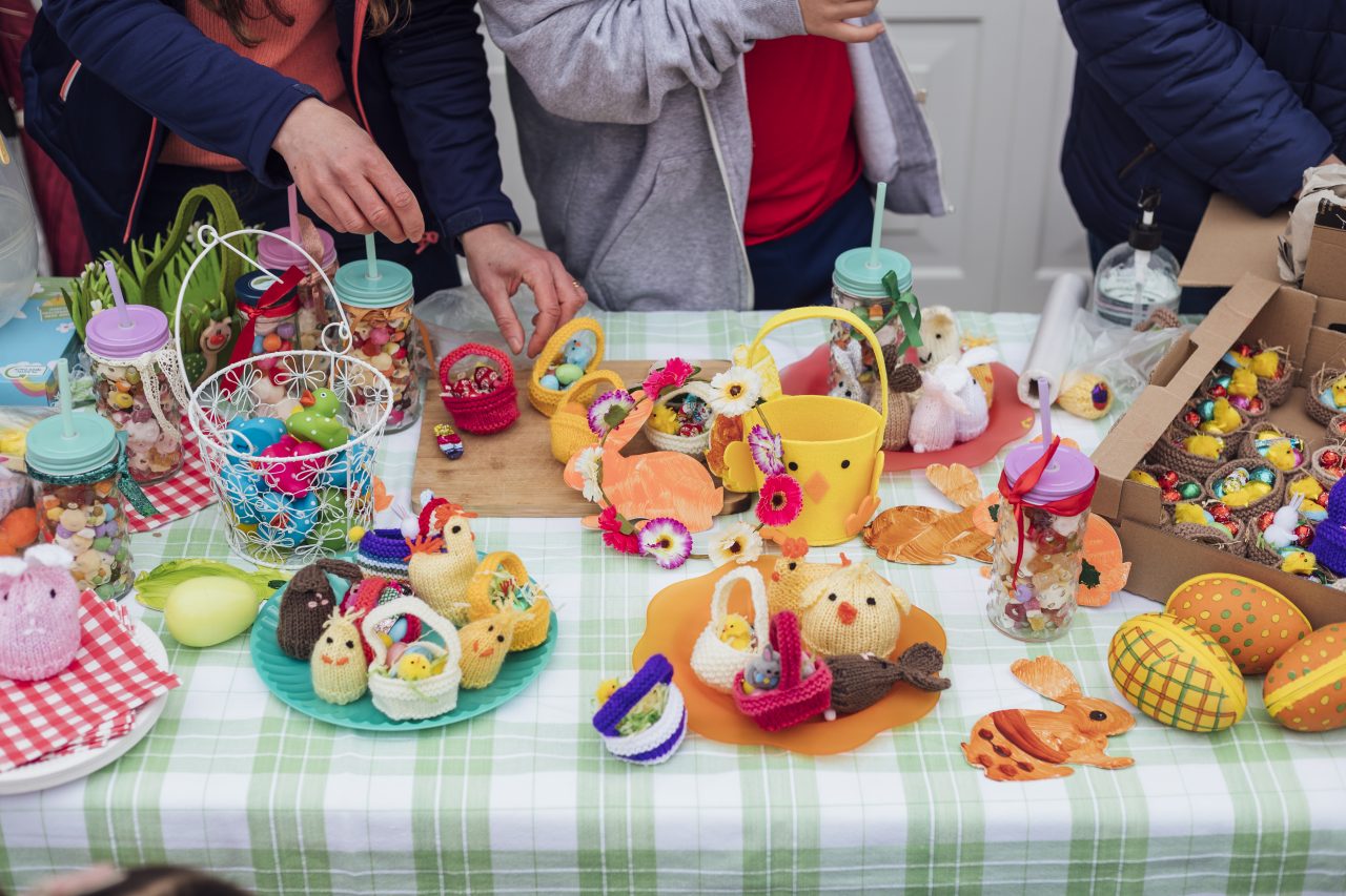Table at an Easter yard sale in a garden in the North East of England. There are hand made easter crafts on a table and chocolate snacks.