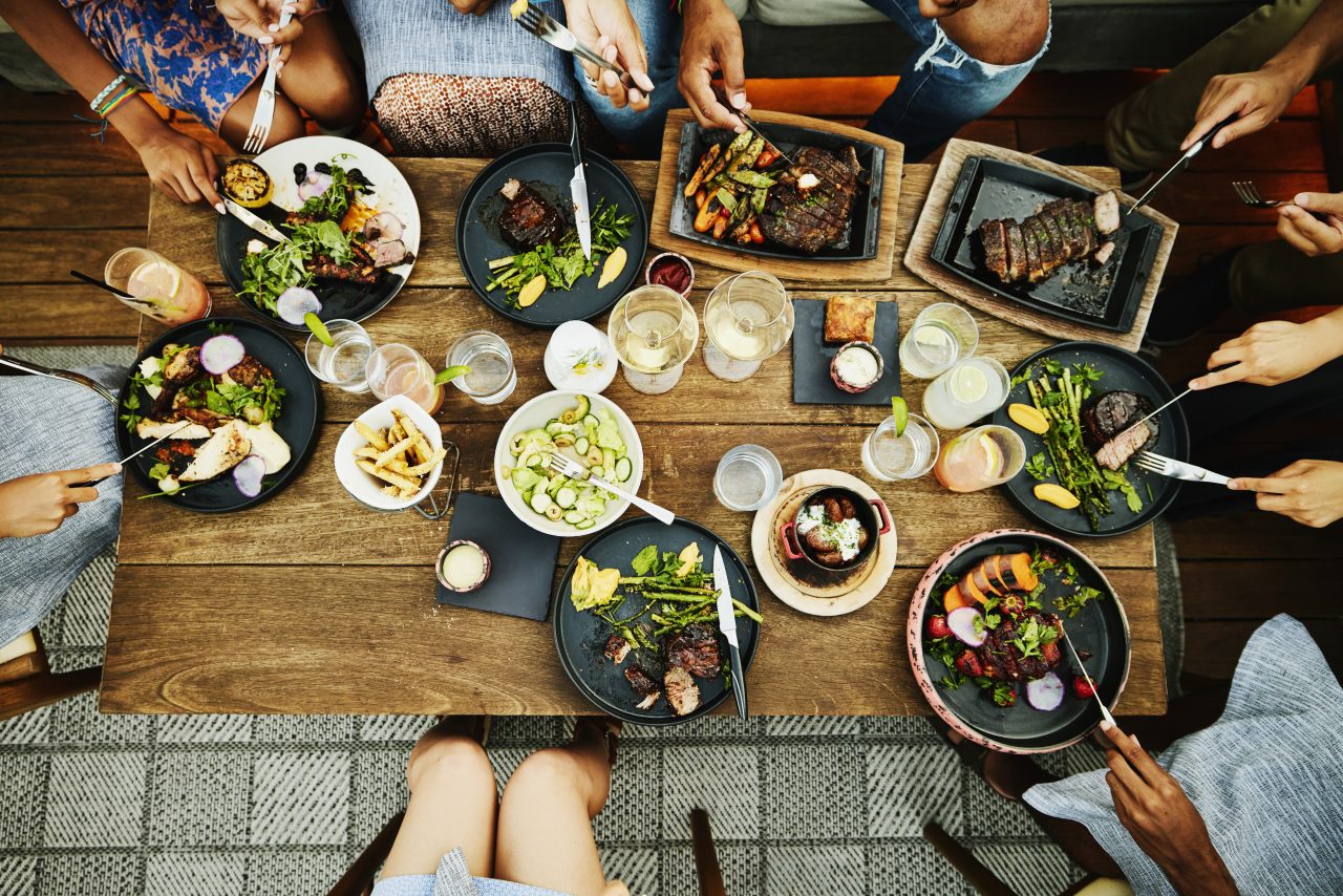 Medium overhead shot of families sharing dinner at table at outdoor restaurant during vacation