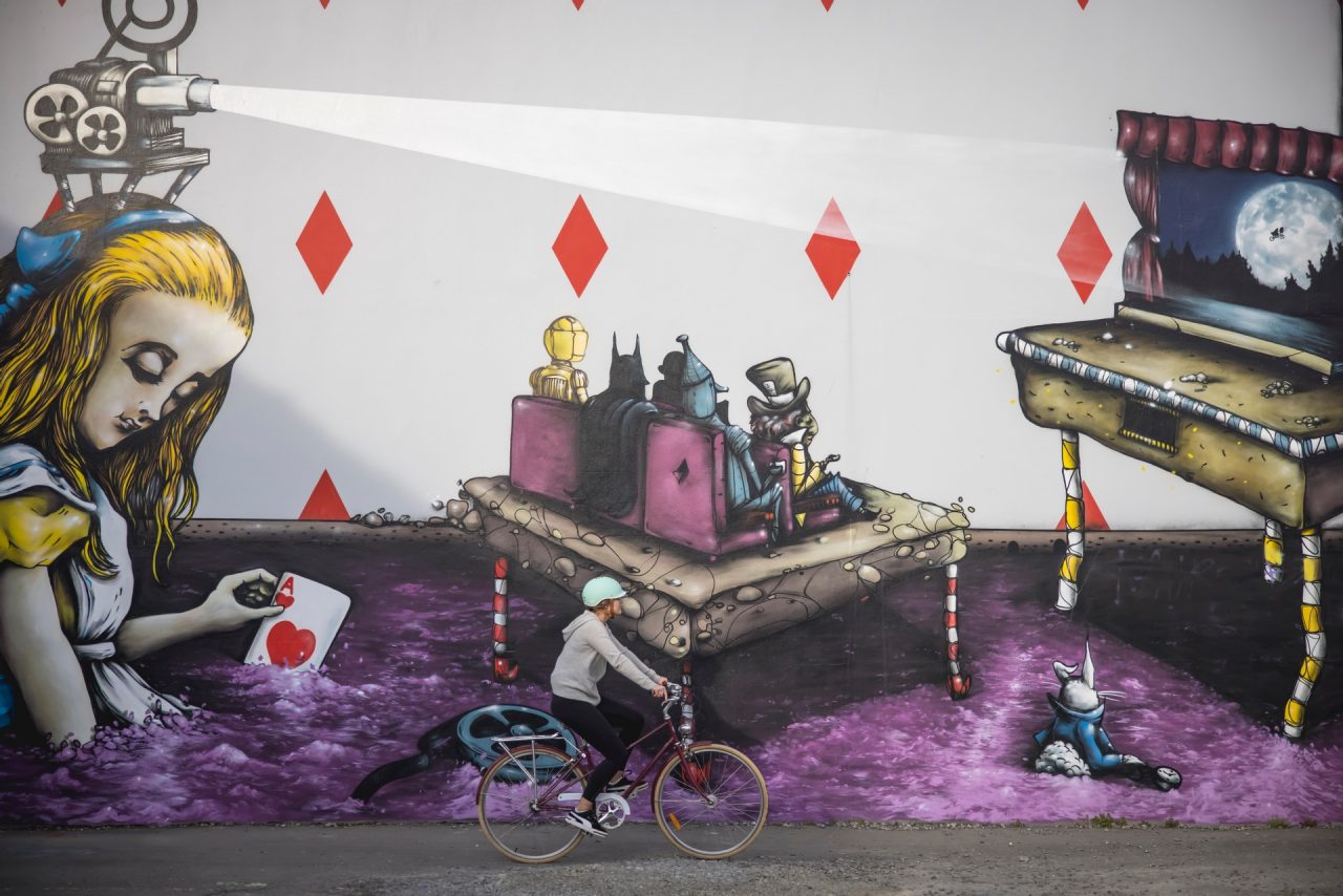 a woman riding a bike in front of an Alice in Wonderland street art mural.