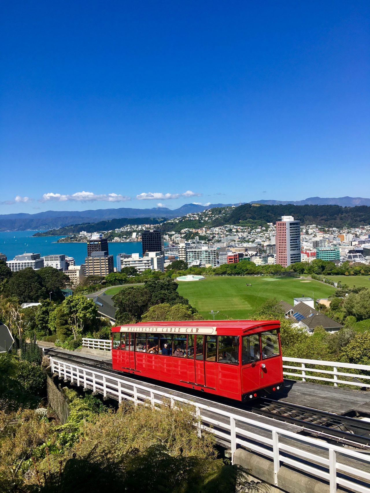 red cable car climbing up a hill that overlooks wellington City