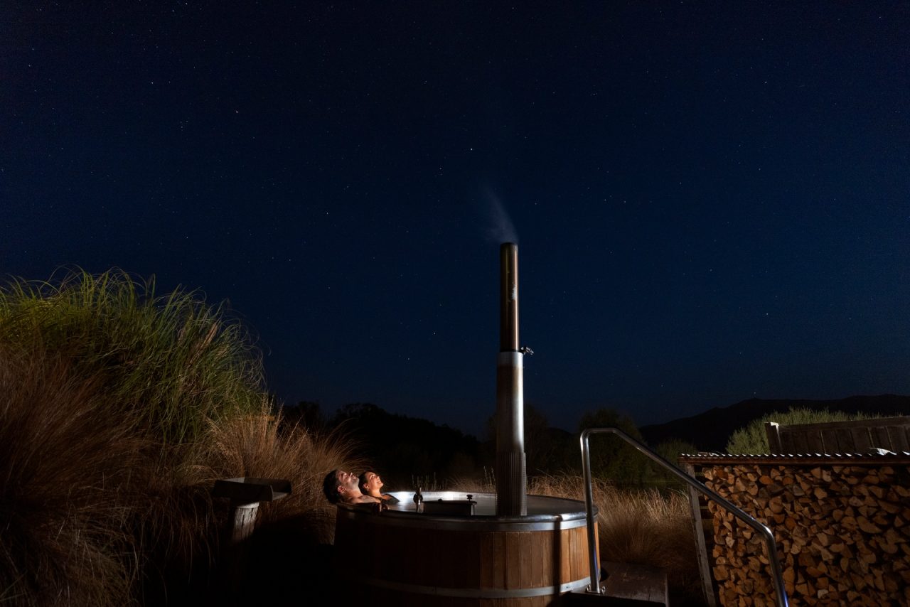 a couple in a wooden hot tub at night looking up at the stars